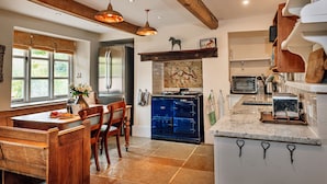 A kitchen with a wooden bench, a blue oven, and pendant lights. - Beili Glas Cottage (Llanfihangel Ystern Llewern)