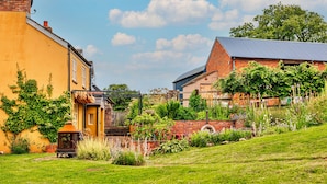 A garden with a brick wall, a yellow building, and a blue-roofed structure. - Beili Glas Cottage (Llanfihangel Ystern Llewern)