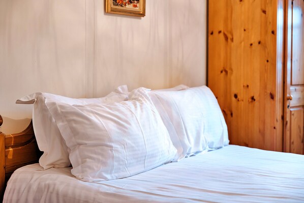 A neatly made bed with white linens in a room with wooden paneling and a framed picture on the wall. - The Onibury (Onibury)
