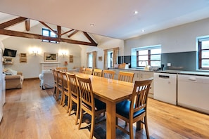 A spacious kitchen with wooden flooring, a large dining table, and white cabinetry.
