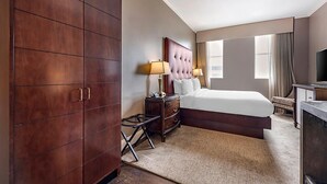 Una habitación de hotel con una cama grande, un armario de madera, una mesita de noche con lámparas y un televisor.