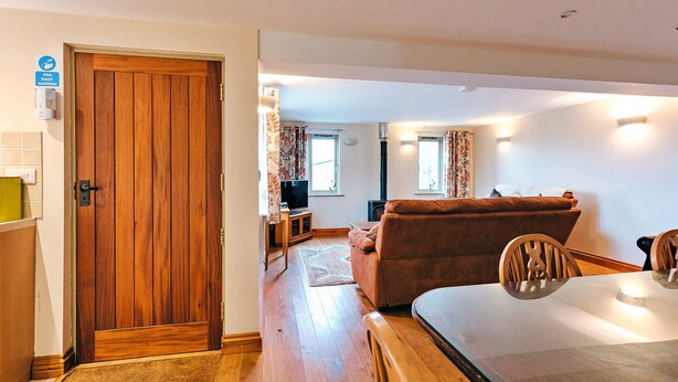 Una habitación con puerta de madera, un sofá, un televisor y una mesa de comedor con sillas.