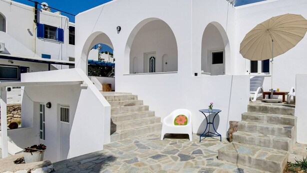 A white building with stone steps, a chair with a cushion, and a table with a flower. - Cozy and comfortable Cycladic home to enjoy hospitality in Dryos of Paros Island (Paros)