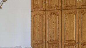 A neatly made bed with white linens and rolled towels, a wooden wardrobe with multiple doors, and a colorful striped blanket. - Cozy and comfortable Cycladic home to enjoy hospitality in Dryos of Paros Island (Paros)