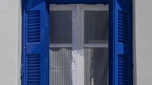 A window with blue shutters, a white wall, and a small decorative item on the sill. - Cozy and comfortable Cycladic home to enjoy hospitality in Dryos of Paros Island (Paros)