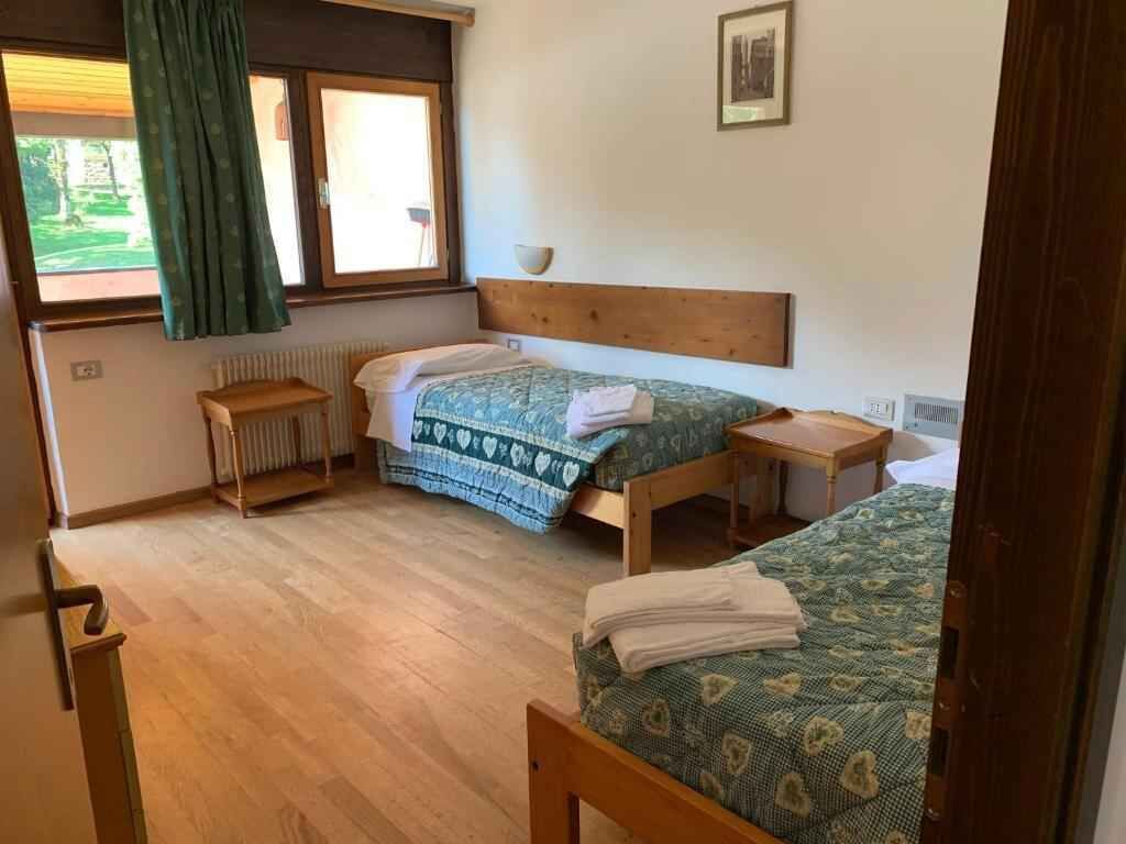 Ein Zimmer mit zwei Betten, einem kleinen Tisch, einem Heizkörper und einem Fenster mit Vorhängen.