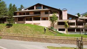 Um hotel com vários andares, telhado inclinado, varandas e uma placa indicando ser um hotel.