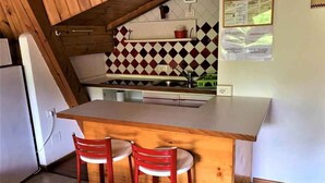 Cozinha com ilha de madeira, dois bancos vermelhos, geladeira branca e painel de fundo xadrez.