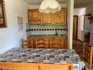 A kitchen with wooden cabinets, a tiled backsplash, a sink, and a dining table with a checkered tablecloth. - Holiday apartment with mountain view (Cavalese)