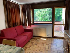 A room with a red sofa, a radiator, a window with a view of greenery, and a tiled floor. - Holiday apartment with mountain view (Cavalese)