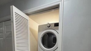 Une buanderie équipée de deux machines à laver et deux sèche-linge superposés, une porte blanche et un sol carrelé.