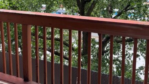 Une terrasse en bois avec une rambarde, un arbre aux feuilles vertes et un ciel bleu dégagé.