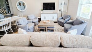 A living room with a sofa, armchairs, a coffee table, a TV, a mirror, and a cabinet.