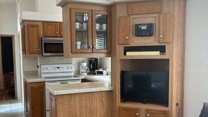 Une cuisine moderne avec des meubles en bois, un four à micro-ondes, une cuisinière et un grand téléviseur à écran plat.