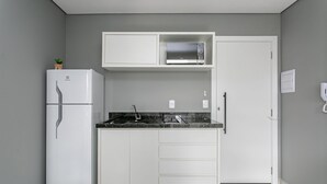 A compact kitchen with a white refrigerator, a microwave, and a sink with a black countertop. - New studio near Beiramar Shopping #HKS25 (Florianópolis)