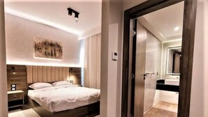 Un dormitori modern amb un llit gran, taules de nit, una obra d'art penjada a la paret i una porta corredissa que dona a un bany.