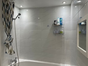 Un baño moderno con ducha, bañera y tocador con repisas para artículos de aseo.