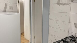 A narrow hallway with white doors, a kitchen area with a gas stove, and marble-patterned walls. - Walk to Lcy Airport/ Excel /dlr 1Br Flat (London)