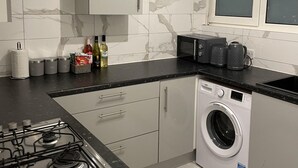 A compact kitchen with a gas stove, a built-in washing machine, and a microwave. - Walk to Lcy Airport/ Excel /dlr 1Br Flat (London)