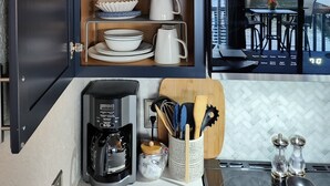 Een keuken met donkere kastjes, een koffiezetapparaat, en uitzicht op een eethoek met terrasmeubels.