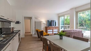 A modern kitchen with a dining area, a television, and a view of greenery outside.