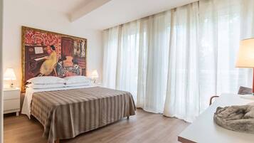 Ein Hotelzimmer mit einem Bett, zwei Nachttischlampen, einem Bild an der Wand und einem Fenster mit leichtem Vorhang.