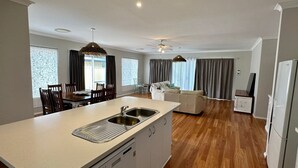A modern kitchen with a central island, a dining area with chairs, a sofa, and a TV stand.