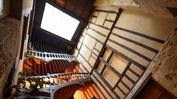 Un escalier étroit avec des rampes en bois, donnant sur une pièce avec une fenêtre et une porte.