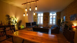 Un salon chaleureux avec une table à manger en bois, un canapé et un téléviseur. On y trouve également des plantes et une cheminée.