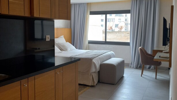 Een moderne hotelkamer met kitchenette, een bed met groot raam, zithoek en televisie.