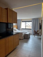 Habitación de hotel moderna con kitchenette, cama con ventana grande, zona de estar y televisor.