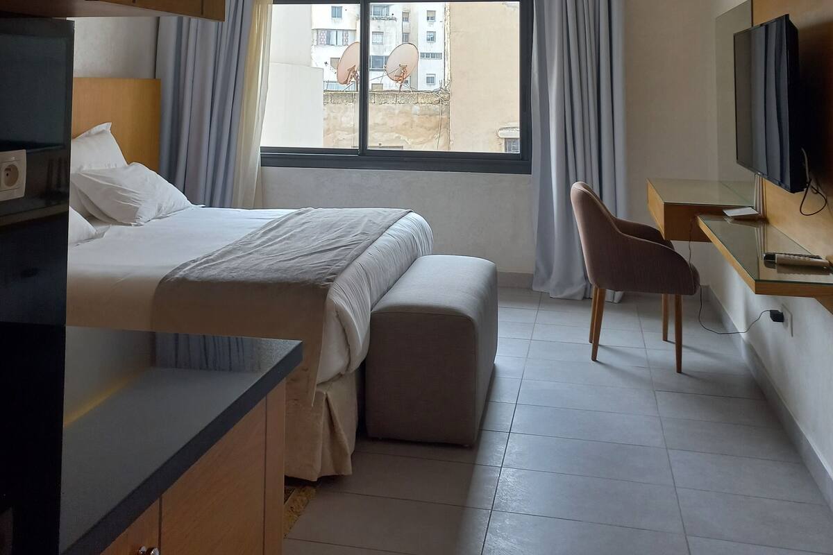 Une chambre d’hôtel avec un lit, un bureau, une chaise, une télévision et une fenêtre avec des rideaux.