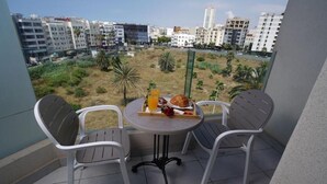 Een balkon met twee stoelen en een tafel, met uitzicht op een stadsbeeld met gebouwen en een grasveld.
