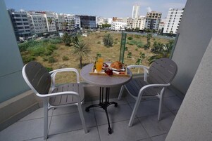 Un balcón con dos sillas y una mesa, con vista a un paisaje urbano que incluye edificios y una zona verde.