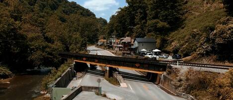 Un pont enjambant une rivière, avec une route en dessous, le tout entouré de collines boisées et de quelques bâtiments.