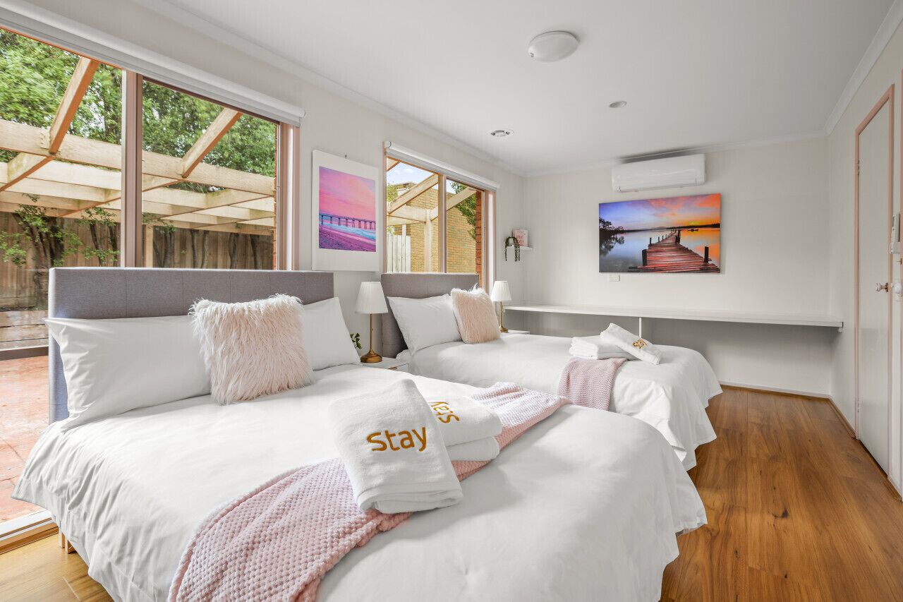 A hotel room with two beds, a large window, and artwork on the wall.