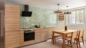 Eine moderne Küche mit Holzschränken, einem eingebauten Backofen, einer Spüle und einem Essbereich mit Holztisch und Stühlen.