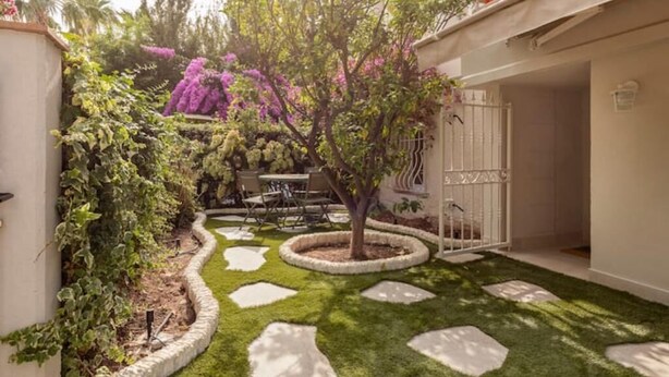 Ein gepflegter Garten mit Baum, trittsteinen und einer Terrassenfläche.