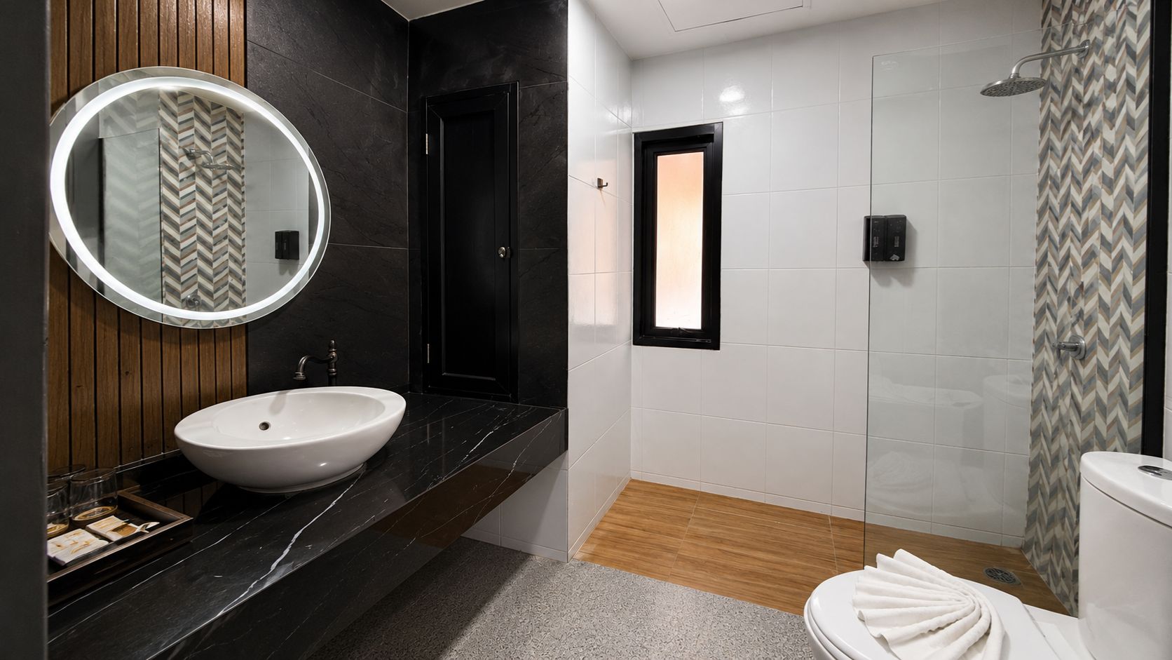 Ein modernes Badezimmer mit rundem Spiegel, Waschbecken in Weiß, Dusche und Toilette.