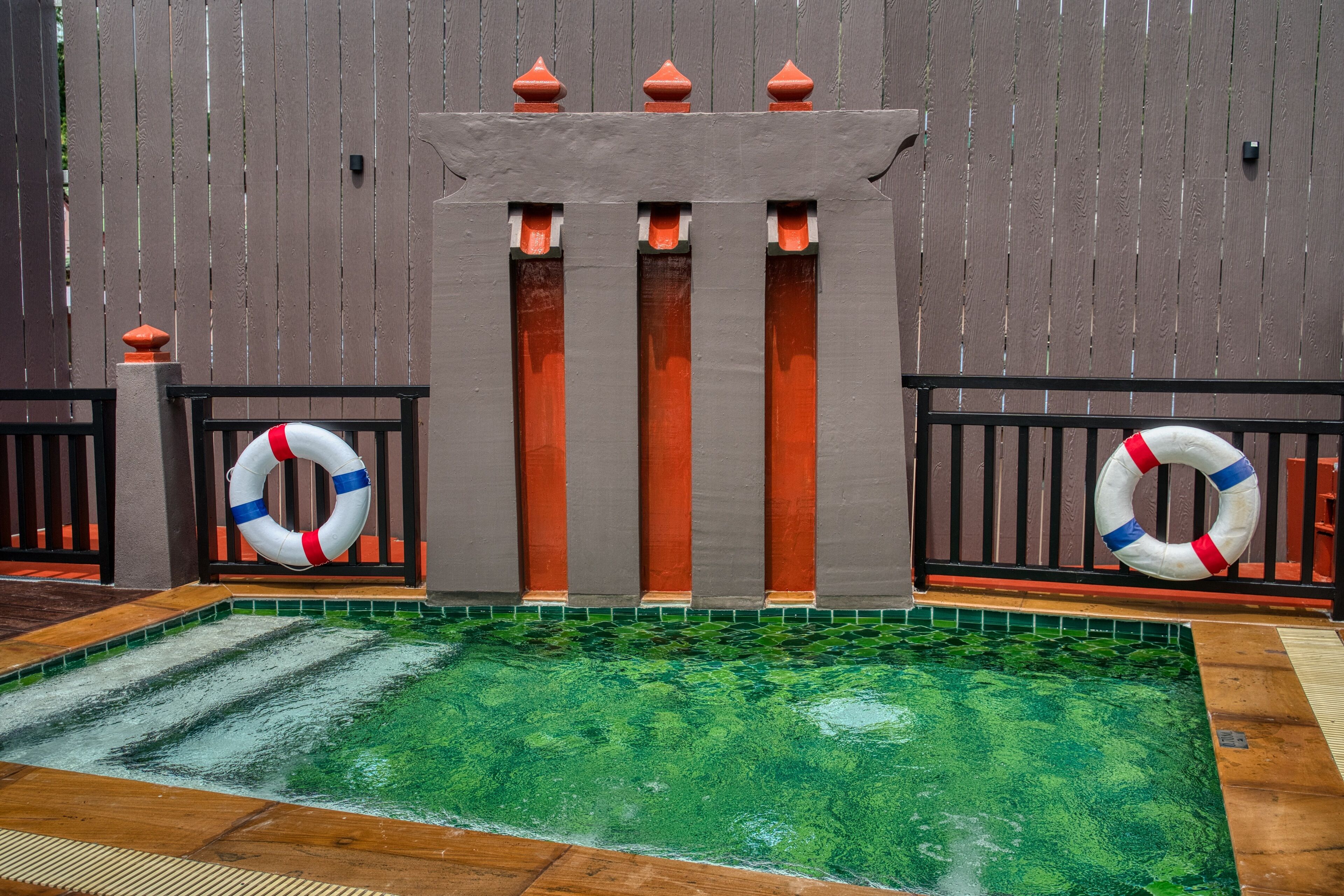 A swimming pool with a wooden fence, lifebuoys, and a tiled floor.
