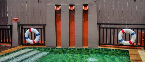 A swimming pool with a wooden fence, lifebuoys, and a tiled floor.
