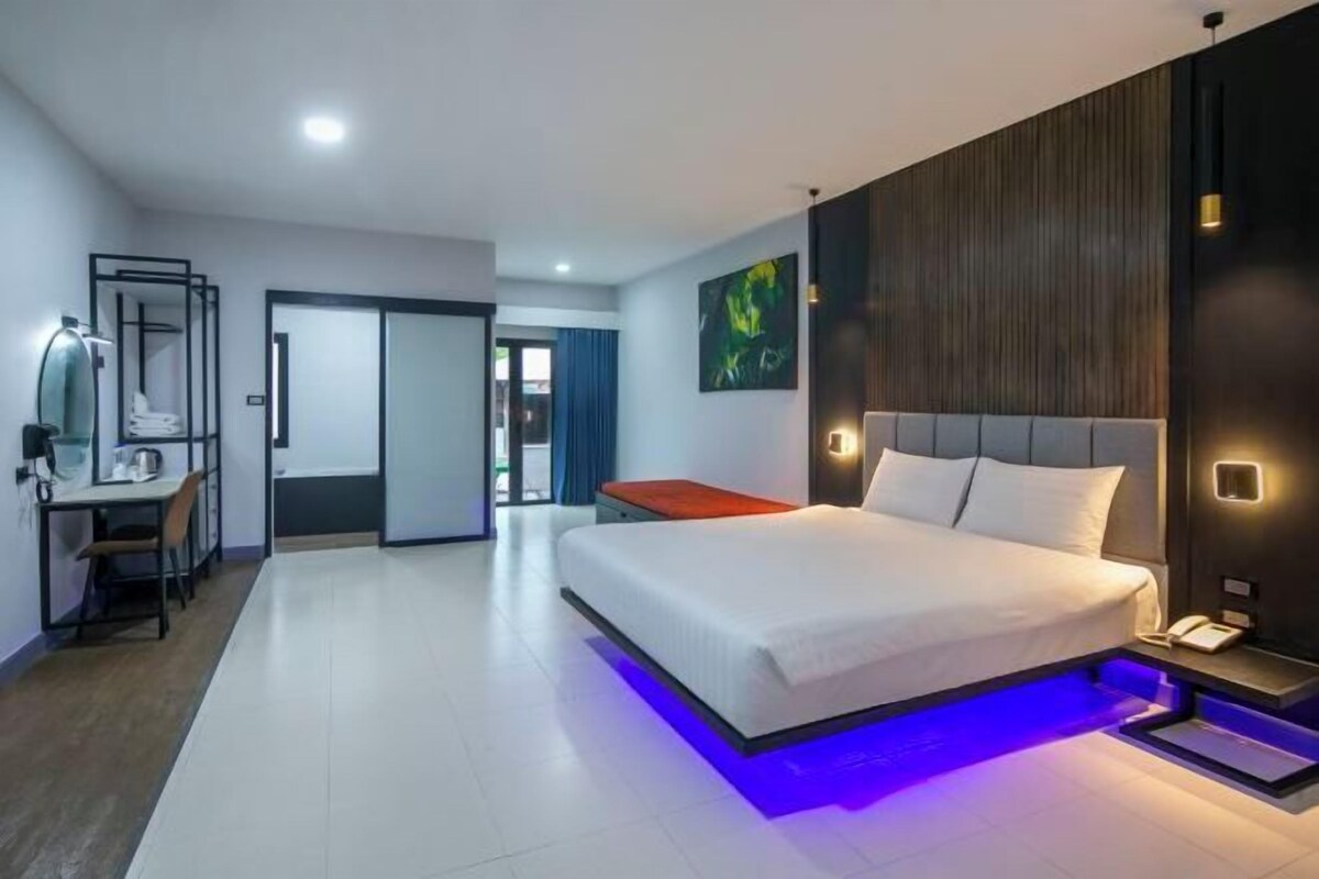 A modern hotel room with a large bed, a desk with a chair, and a wardrobe.