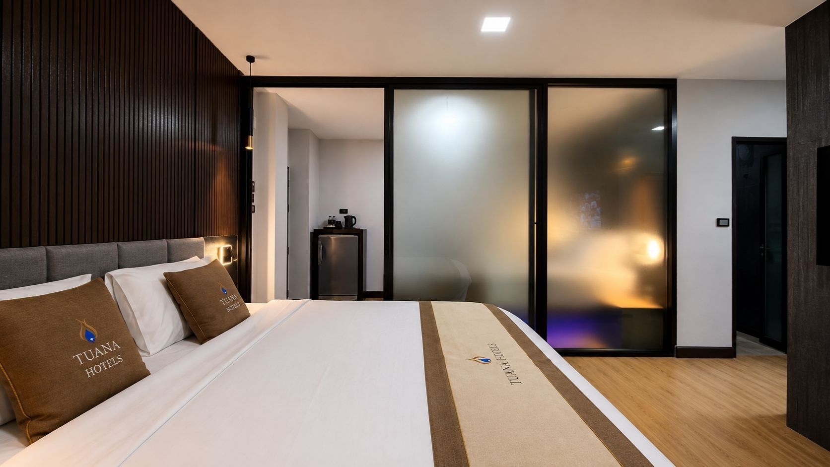 Habitación de hotel moderna con una cama grande, un mini bar y un ventanal corredero que da a un balcón.