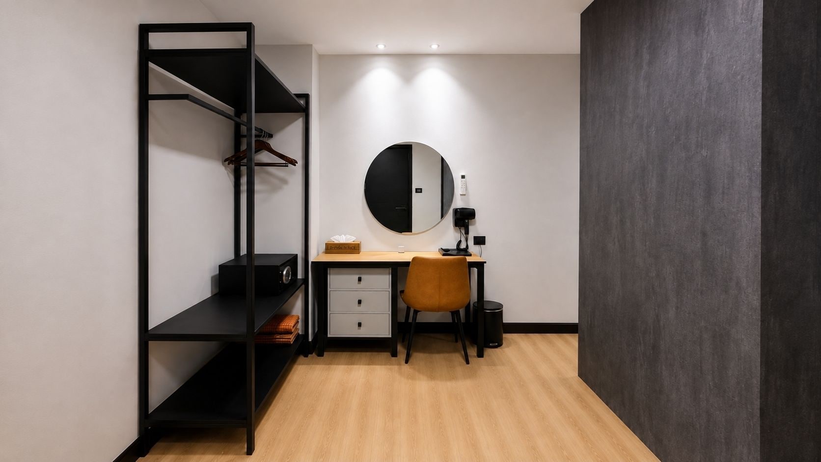 A compact bedroom with a bed, a desk, a chair, a wardrobe, and a round mirror.