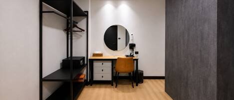 A compact bedroom with a bed, a desk, a chair, a wardrobe, and a round mirror.
