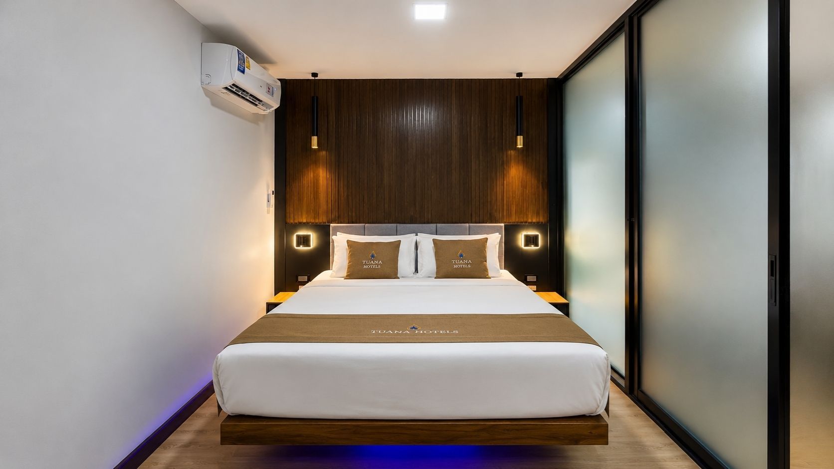 A hotel room with a large bed, a wall-mounted air conditioner, and a wooden headboard.