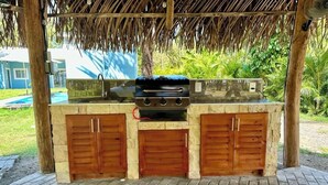 An outdoor barbecue area with a stone countertop, a grill, and wooden cabinets. - Villa Cielo, Casa de Playa Frente al mar (Provincia de Puntarenas)