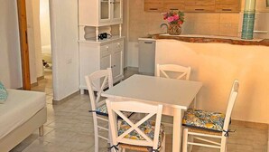 A compact kitchen with white cabinets, a dining table with chairs, and a hanging light fixture. - Villa Rosa dei Venti (Valledoria)