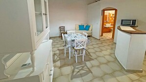 A dining area with a table and chairs, a kitchen with a microwave, and a doorway leading to another room. - Villa Rosa dei Venti (Valledoria)