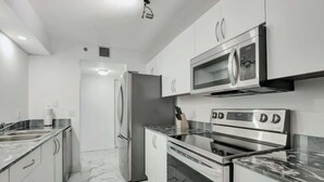 Una cocina moderna con electrodomésticos de acero inoxidable, armarios blancos y encimera de mármol.